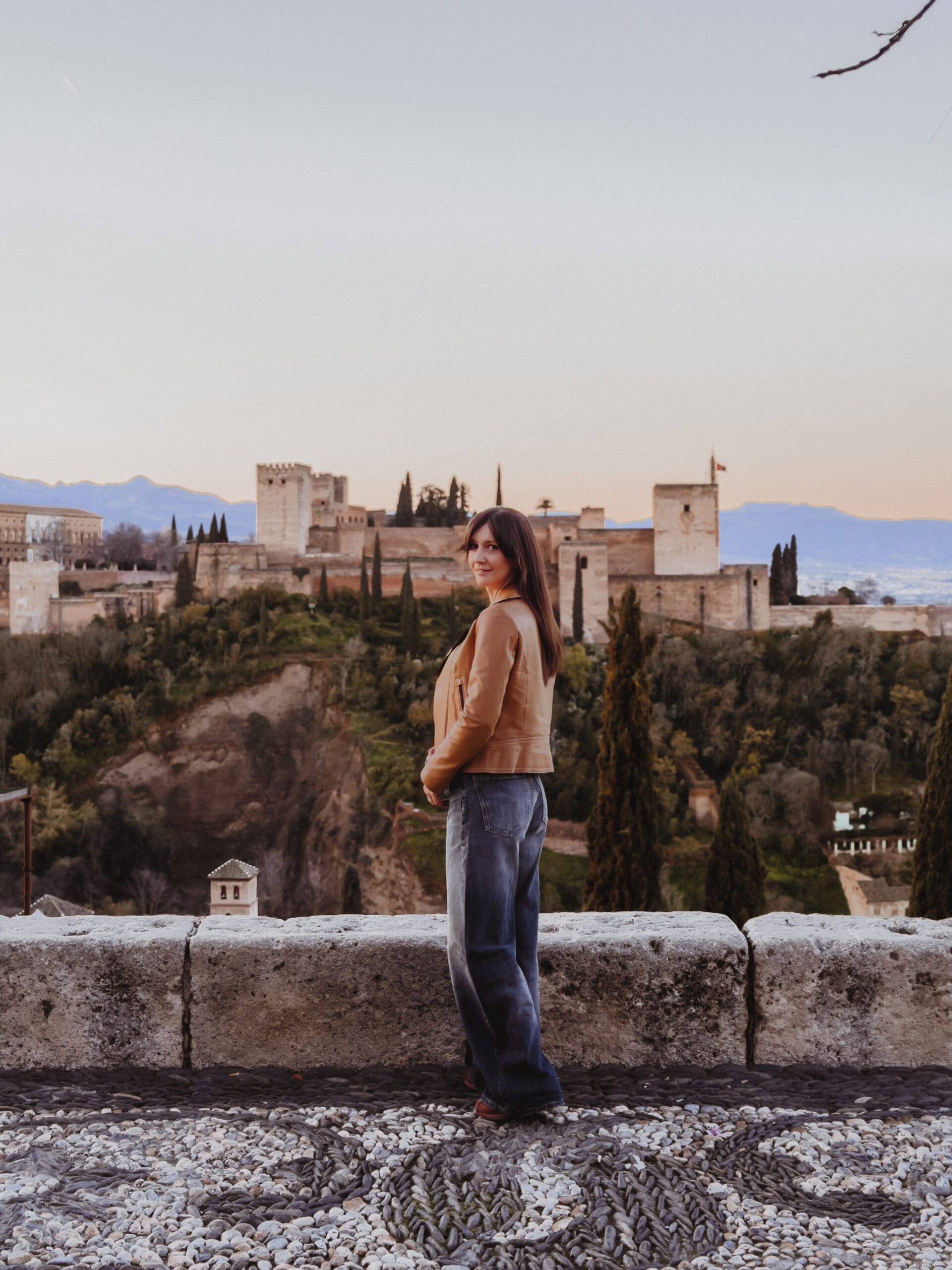 Woman in a leather jacket at Mirador de San Nicolás at sunrise, Alhambra behind her — Granada luxury travel guide and best viewpoints.